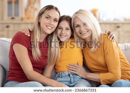 Family portrait of happy beautiful blonde loving mother, grandmother and child preteen girl at home. Cute child daughter hugging her mom and granny, posing on couch for family picture