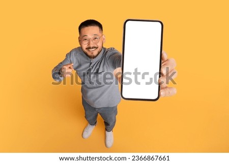 Check This. Smiling Asian Man Pointing At Big Blank Smartphone In His Hand, Happy Millennial Guy Advertising Online Offer Or Mobile App, Standing Over Yellow Studio Background, Collage, Mockup Royalty-Free Stock Photo #2366867661