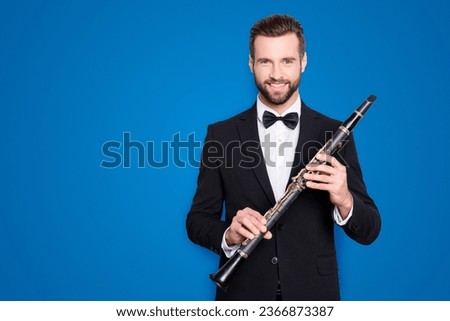 Portrait with copyspace, empty place of stylish cheerful man with hairstyle in black tux holding bassoon in hands, looking ta camera, isolated on grey background Royalty-Free Stock Photo #2366873387