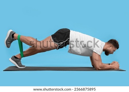 Young man exercising with elastic resistance band on light blue background