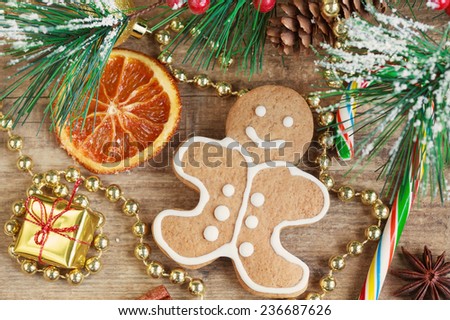 Homemade christmas painted gingerbreads (gingerbread man and red present) on the wooden background with Christmas decorations, cones and candied orange. Selective focus on the man. Toned