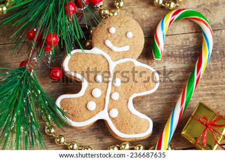 Homemade christmas painted gingerbreads (gingerbread man and red present) on the wooden background with Christmas decorations, cones and golden present. Selective focus on the man. Toned