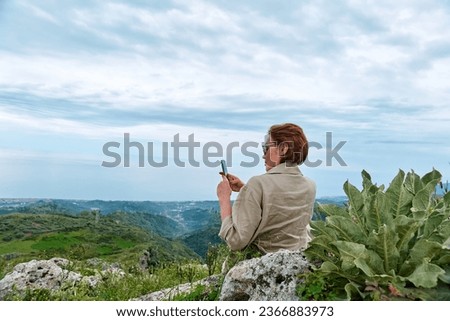 Woman traveler using smartphone to take photo during the trekking in mountain. Mental health, wellbeing, trip adventure and healthy lifestyle.