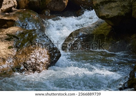 Mountain river with rapids and pristine azure water flowing fast among boulders and rocks with moss