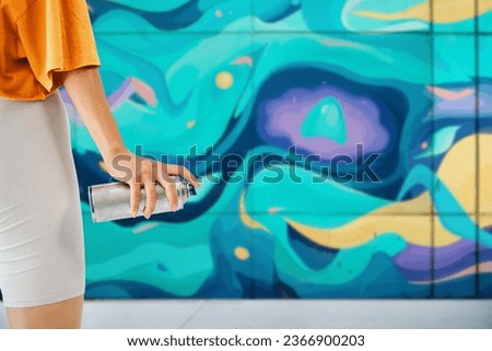 Street artist with spray paint can in hand standing near the wall with her paintings. Copy space. Cropped image. Street art concept