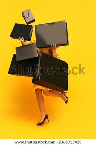 Woman in stylishly outfit carrying a lot of purchases, black shopping paper bags over yellow studio background. concept of fashion, beauty, salesperson, Black Friday, sale. copy space. ad