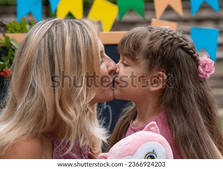 Cute little girl kissing mom, showing love and affection, smiling mother and funny little preschool daughter having fun outside