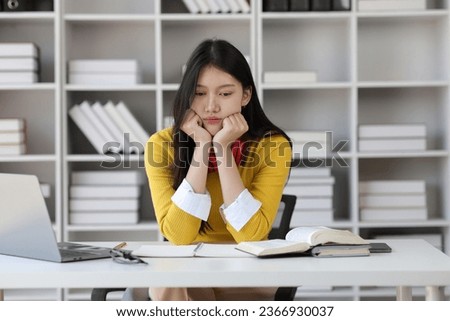 Serious Asian female student reading books for exam preparation in university library.