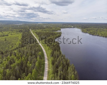 Drone photo of curvy road with forest around it. Finland majestic nature. Sunny early summer day. Birds eye view of the Finland's amazing forests and lakes. 