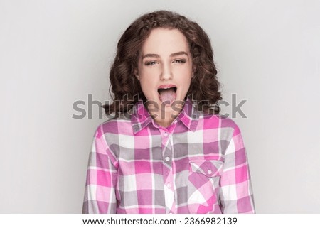 Disgusted pretty woman sticking out tongue, expressing her dislike or disregard towards something, showing tongue at camera as if teasing someone. Indoor studio shot isolated on gray background. Royalty-Free Stock Photo #2366982139