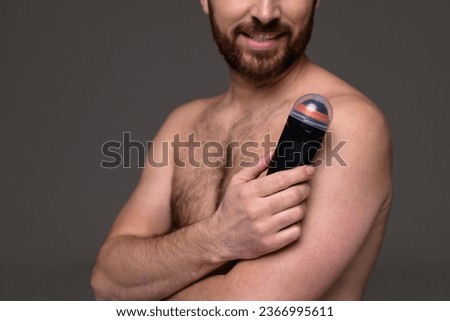 Partial view of shirtless and smiling man holding roll-on deodorant isolated on grey