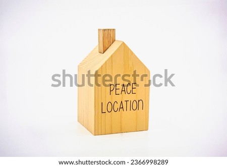 A small single-storey house model made of wood with the words "peace location" written on it. Photograph.