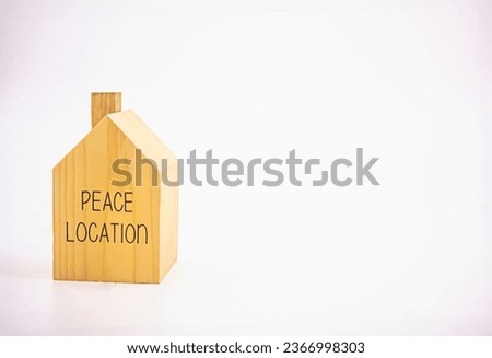 A small single-storey house model made of wood with the words "peace location" written on it. Photograph.