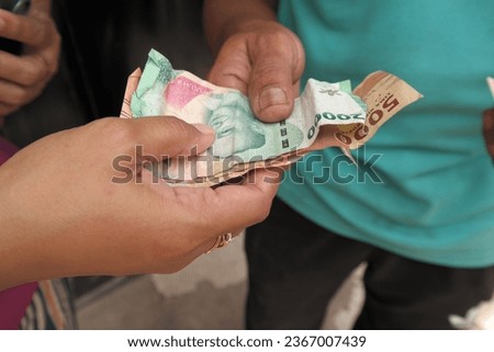 Two hands, one Asian man and woman handing over Indonesian banknotes to each other. Concept of tourist business profit, foreign investment in Indonesia, paying for the goods. 20,000 and 5,000 rupiah