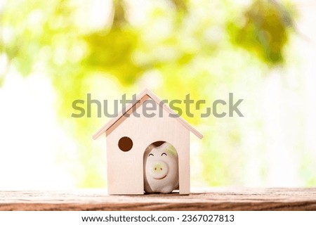 Piggy bank put in the wooden home model put on the wood on nature bokeh in the public park, Loan or save money for buy a house and real estate concept