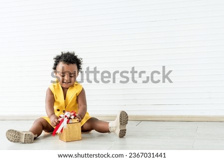 Portrait images, A 2-year-old Nigerian baby girl with beautiful curly hair, smiling and happy with gift box, on white background. to African baby and gift box concept.