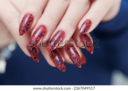 Female hand with long nails and a bright red and blue manicure holds a bottle of nail polish