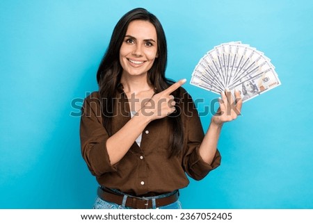 Photo of sweet good mood girl dressed brown shirt pointing finger money fan isolated blue color background