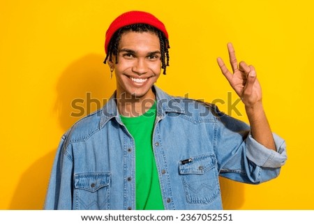 Photo of funny friendly guy dressed denim jacket beanie showing v-sign smiling isolated yellow color background