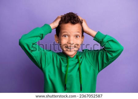 Photo of impressed funky little boy dressed green hoodie arms head smiling isolated purple color background Royalty-Free Stock Photo #2367052587