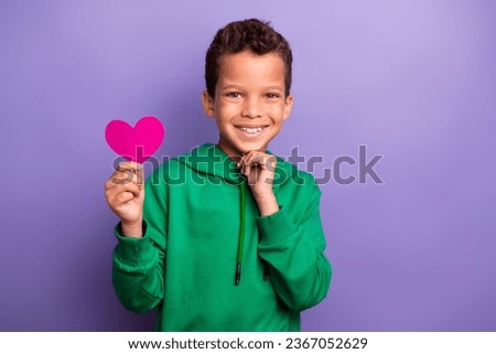 Photo of charming thoughtful little boy dressed green hoodie arm chin rising pink paper heart isolated purple color background Royalty-Free Stock Photo #2367052629