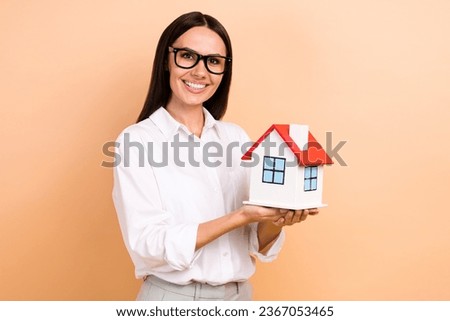 Photo of charming positive girl toothy smile hands hold demonstrate small house isolated on beige color background