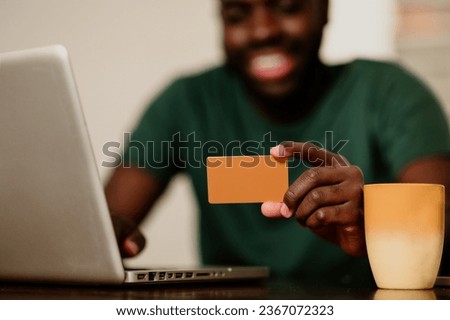 Cropped picture of a multiracial man holding a credit card and typing on a laptop while sitting at home. Hands of a millennial man holding a credit card and typing on a laptop.