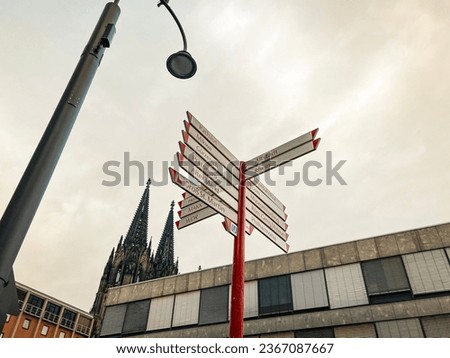 Directional landmarks sign pointing to area attractions in Cologne, Germany. The majestic Cologne Cathedral stands tall in the background of view.