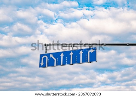 Blue lane traffic sign against a sky with clouds. Turn, U-turn, straight ahead.