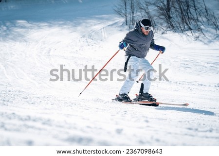 Confident skier skiing downhill in high mountains. Handsome, fashionable man in full sports equipment being photographed in movement on ski slope. Experienced male skier skiing in the mountains. Royalty-Free Stock Photo #2367098643