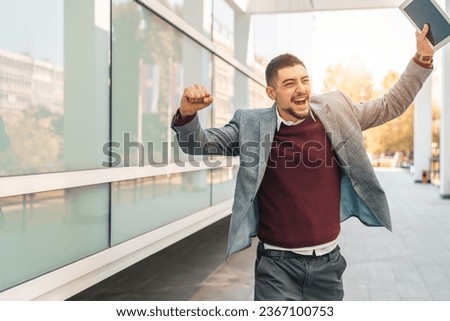 Young successful businessman running while holding digital tablet outdoors. Devoted man expressing excitement and pride about his achievements. Royalty-Free Stock Photo #2367100753
