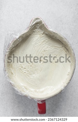 Greek yogurt in a white bowl covered with plastic wrap, process of making Greek yogurt, strained yogurt in ceramic white bowl