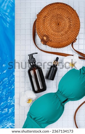 Body oil, orchid, green swimsuit, beach woven bag on a pool background. Body care product after the pool. Body lotion mockup with SPF. Cocktail by the pool. Safe tanning oil for body. 