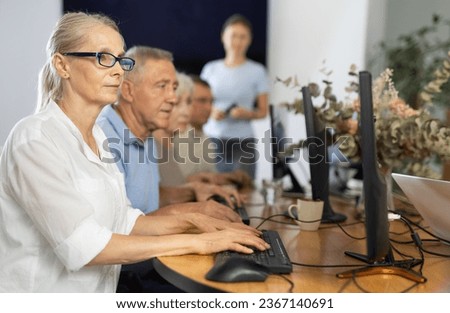 Concerned old woman sitting at computer while trainer speaking on the background
