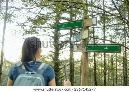 A young woman hiker observes a sign with arrows to follow the correct trail during a nature hike