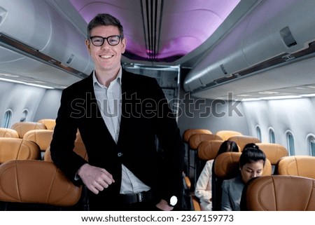 Portrait of happy smiling businessman in black suit, standing on aisle inside airplane, male passenger traveling on business trip by aircraft, businesspeople traveling with airline transportation. Royalty-Free Stock Photo #2367159773