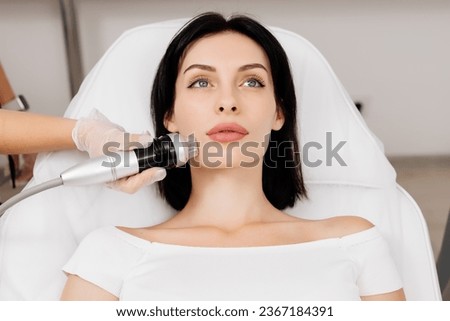 Close-up of a young girl undergoing fractional radiofrequency facelift at a medical center, skin rejuvenation concept. Cosmetic procedures advertising concept. Royalty-Free Stock Photo #2367184391