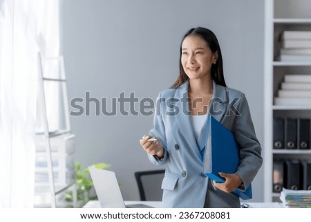 Happy Asian woman holding clipboard at office. Attractive and cute Asian businesswoman thinking up new ideas and holding clipboard at office.