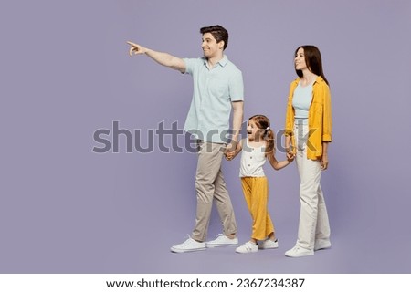 Full body side view young parents mom dad child kid daughter girl 6 years old wearing blue yellow casual clothes hold hands walk go point aside isolated on plain purple background. Family day concept