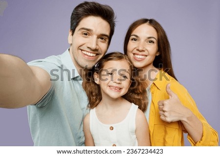 Close up young fun happy parents mom dad with child kid daughter girl 6 year old wear blue yellow casual clothes do selfie shot pov mobile cell phone show thumb up isolated on plain purple background