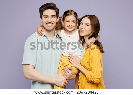 Side view young smiling fun happy parents mom dad with child kid girl 6 years old wear blue yellow casual clothes hold daughter looking camera isolated on plain purple background. Family day concept