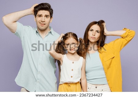 Young shocked sad amazed parents mom dad with child kid daughter girl 6 years old wear blue yellow casual clothes look camera hold scratch head isolated on plain purple background. Family day concept Royalty-Free Stock Photo #2367234427