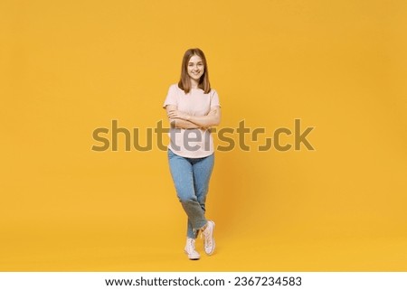 Full length of young confident smiling student woman 20s wear casual basic pastel pink t-shirt, jeans looking camera, holding hands crossed folded isolated on yellow color background studio portrait Royalty-Free Stock Photo #2367234583