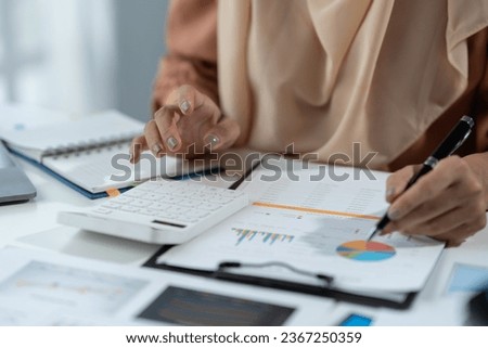 Motivated muslim businesswoman wearing hijab working on real estate project analyzing document data graph discussing presentation work income calculation tax to company in office.