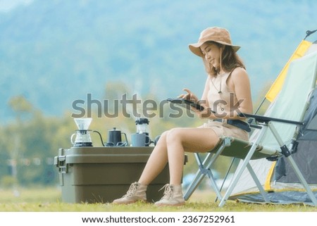 An Asian female sits and relaxes listening to music while camping vacation and drinks coffee outdoors. copy space. Slow life. Enjoying the little things. spends time in nature in summer.