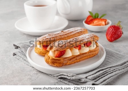 Eclairs with cream and fresh strawberries sprinkled with powdered sugar on top on a gray concrete background Royalty-Free Stock Photo #2367257703