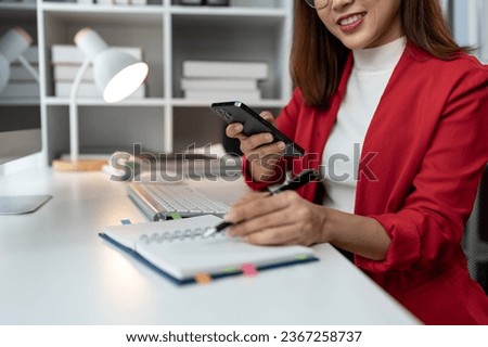 Asian businesswoman holding a smartphone using a calculator to calculate on graph paper Work record Budget calculations, taxes, financial accounts placed on the table in the office Management concept