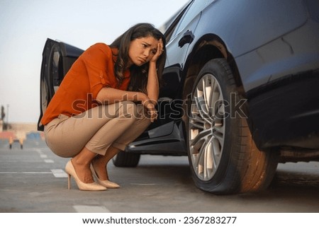 Portrait of a despair woman crouching next to her car with flat tire, problems on the road, deflated tire. Royalty-Free Stock Photo #2367283277