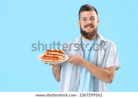 Portrait of happy young man with tasty hot dogs on plate against blue background