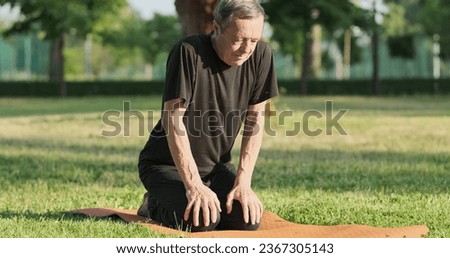 Back hurts, warm-up for health, arch back, tilt look forward. Senior man engaged in physical exercises on mat grass in city park in summer morning